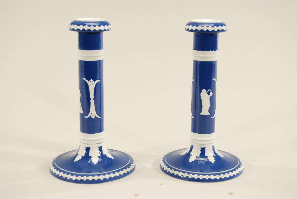 This pair of porcelain candlesticks is in the Wedgwood style of Jasperware but these have a bright glaze. The applied white decorative elements contrast beautifully with the blue glaze and have a lovely neoclassical elegance. These have a nice
