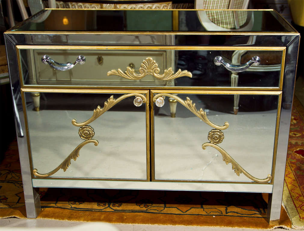Pair of charming vintage Hollywood Regency style dressers, circa 1940, overall mirrored with distress-painted wood frame, the enclosed case with a single drawer over a two-door cabinet, both with bronze-scroll decoration. By John Stuart.