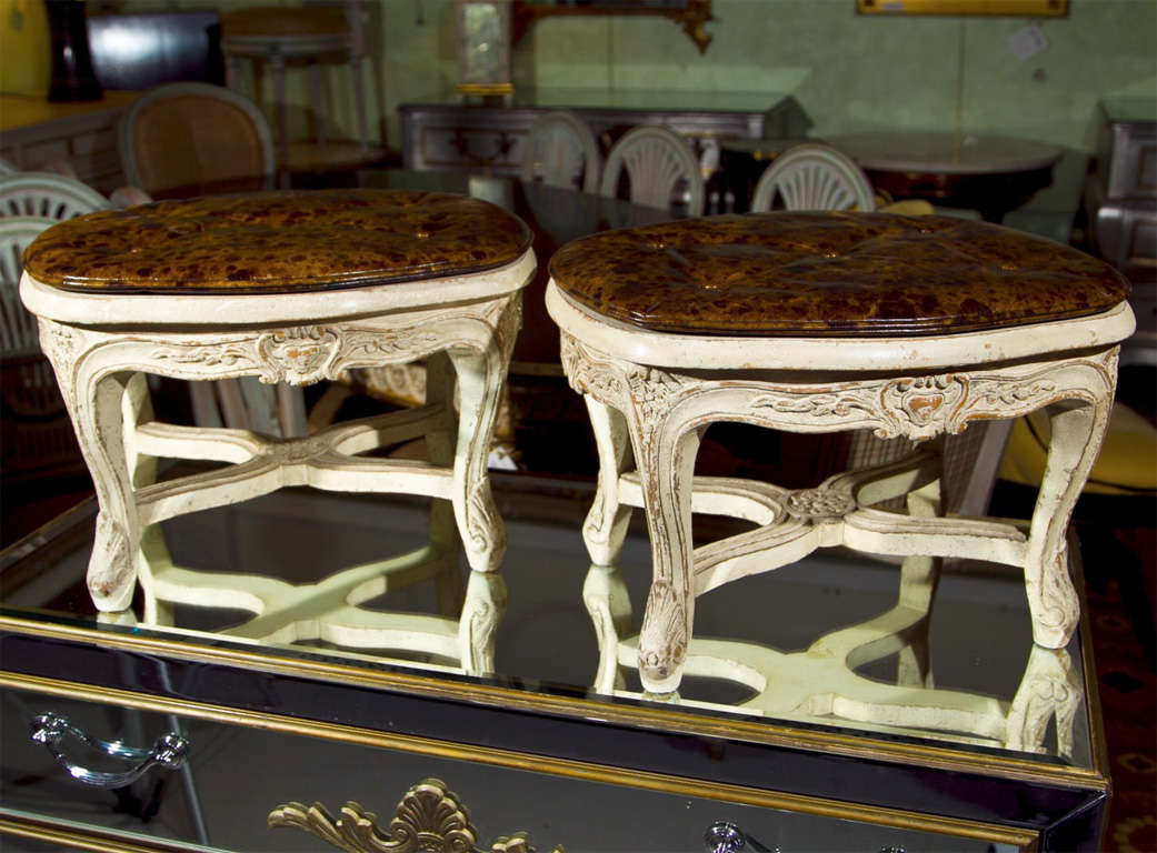 Pair of French Louis XV style low footstools, the white distress-painted frame with brown worn leather cushion over a caned top.