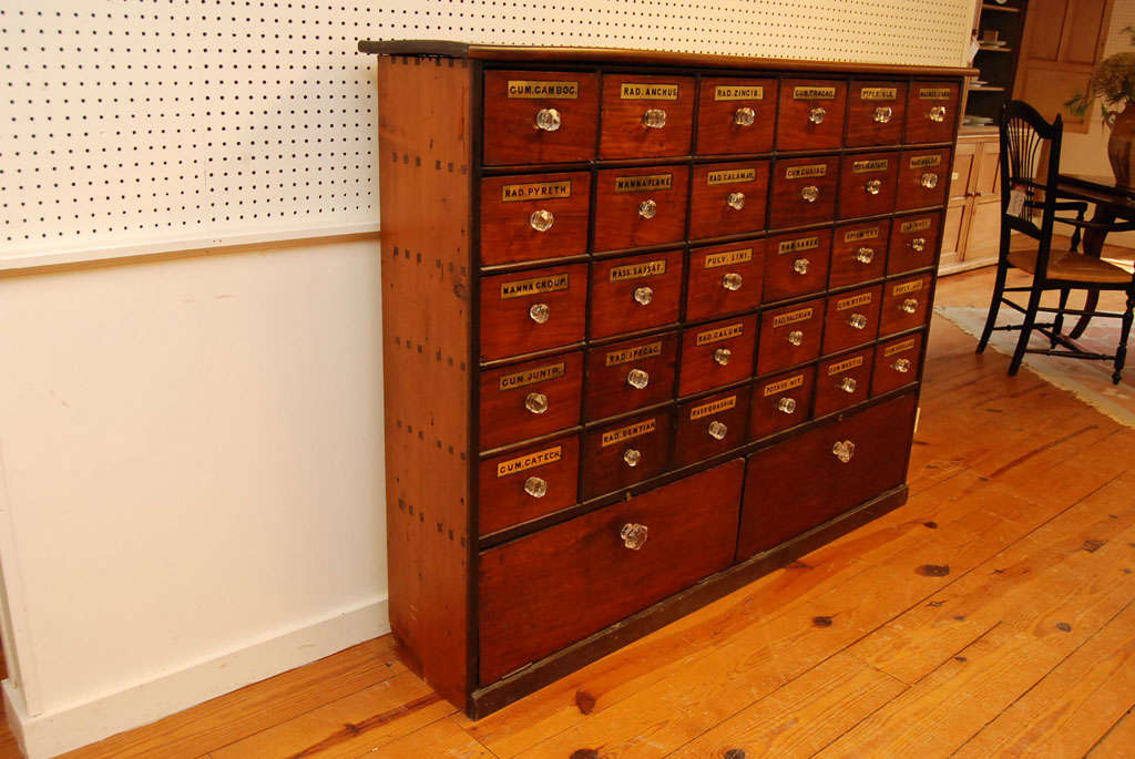 This is an exceptional example of an authentic English apothecary. it has original brass labels which are recessed on each of its thirty drawers, each with a glass knob pull. At the bottom are two storage areas, also with glass pulls that drop down