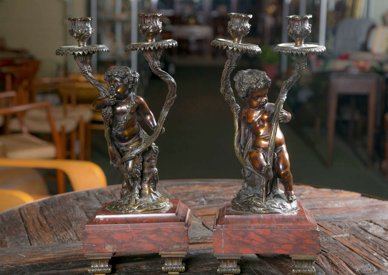 A pair of French Rococo style candelabra after Claudion.  Bronze set upon rouge marble base.