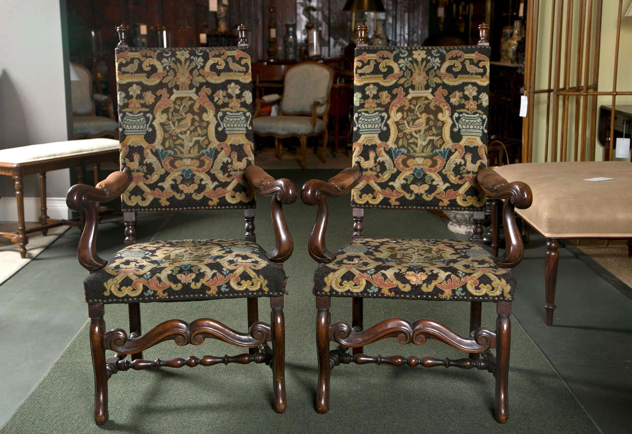 A pair of English Jacobean style carved walnut armchairs with carved, rolled arms, vase finials and a curved center stretcher. Covered in 19th century tapestry.