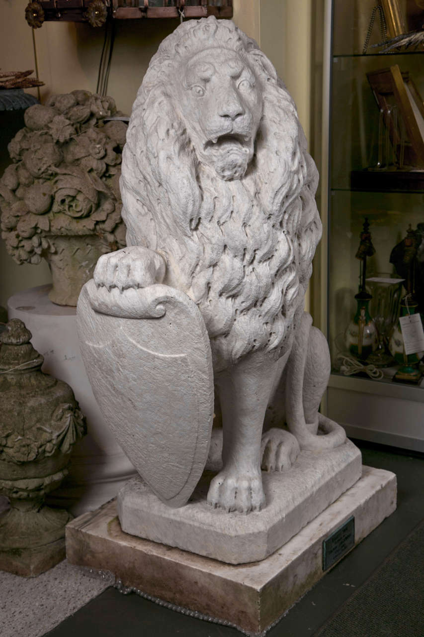A pair of finely carved and modeled Carrara marble armorial lions. These were carved in Carrara, Italy in 1889 by Elerio Panzeroni. They are mounted on marble plinths with a bronze plaque.