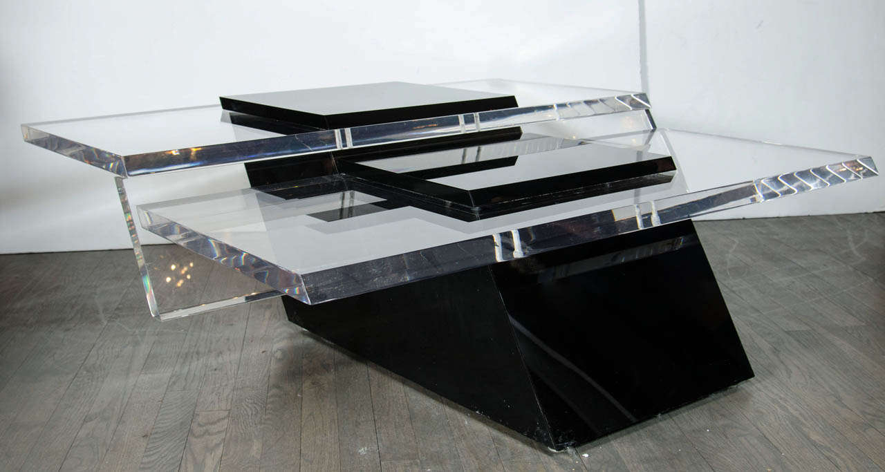 This outstanding multi-level lucite cocktail table will be a truly interesting statement in any space. It features black lucite angular blocks as its base,a cantilever design and a thick top made of clear lucite.