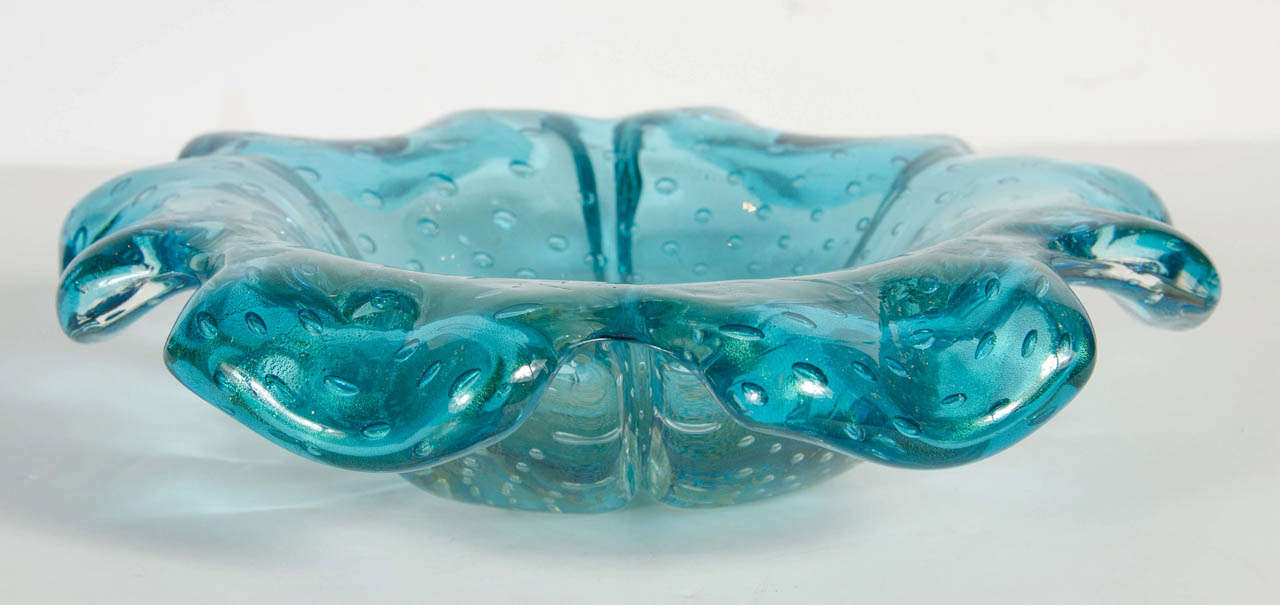 This gorgeous bowl is hand blown Murano glass in a rich turquoise color with 24k gold flecks and murines throughout . It has a stylized floral form design and would be a great accent piece.