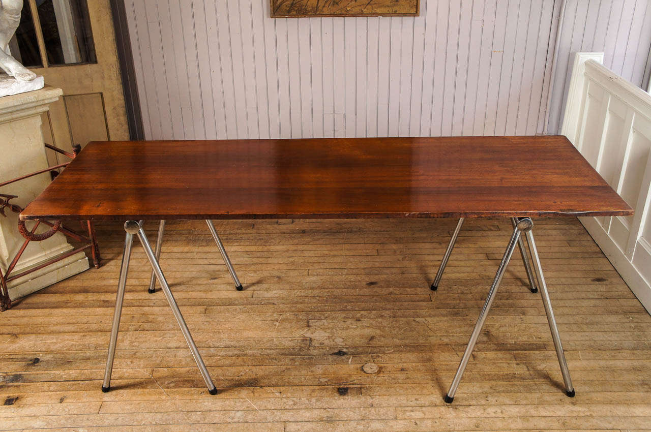 pair of mid century chrome sawhorses support large mahogany free floating top
