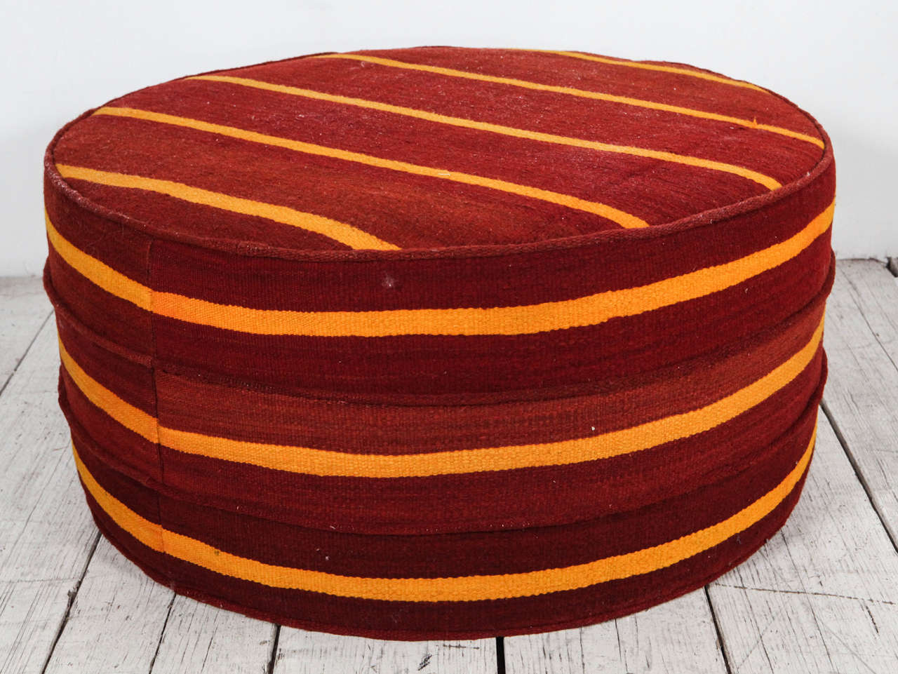 Large round ottoman in red and gold vintage kilim with three rings of piping around circumference.