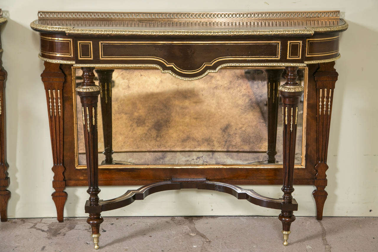 A Pair of Louis XVI Style Console Pier Tables attributed to Jansen. The finely bronze mounted French legs supporting a mirrored back flanked by bronze decorated fluted legs. The front legs having bronze sabots terminating in bronze caps with fluted