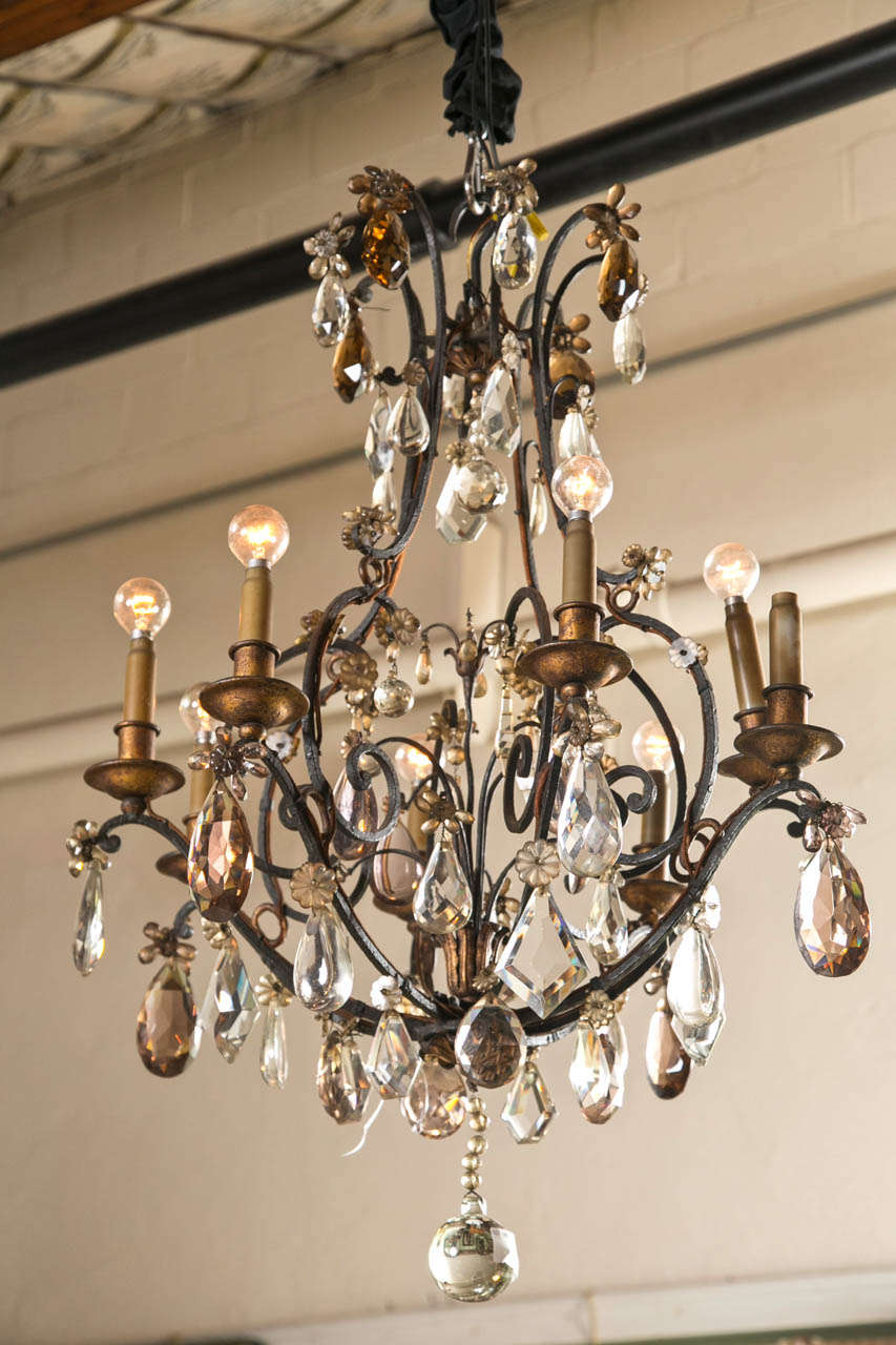 A chandelier by Maison Jansen, circa 1900s. This eight-light chandelier having deep swooping arms with attached crystals and colored crystals though out. The frame of wrought iron. An older piece from one of France finest designers.