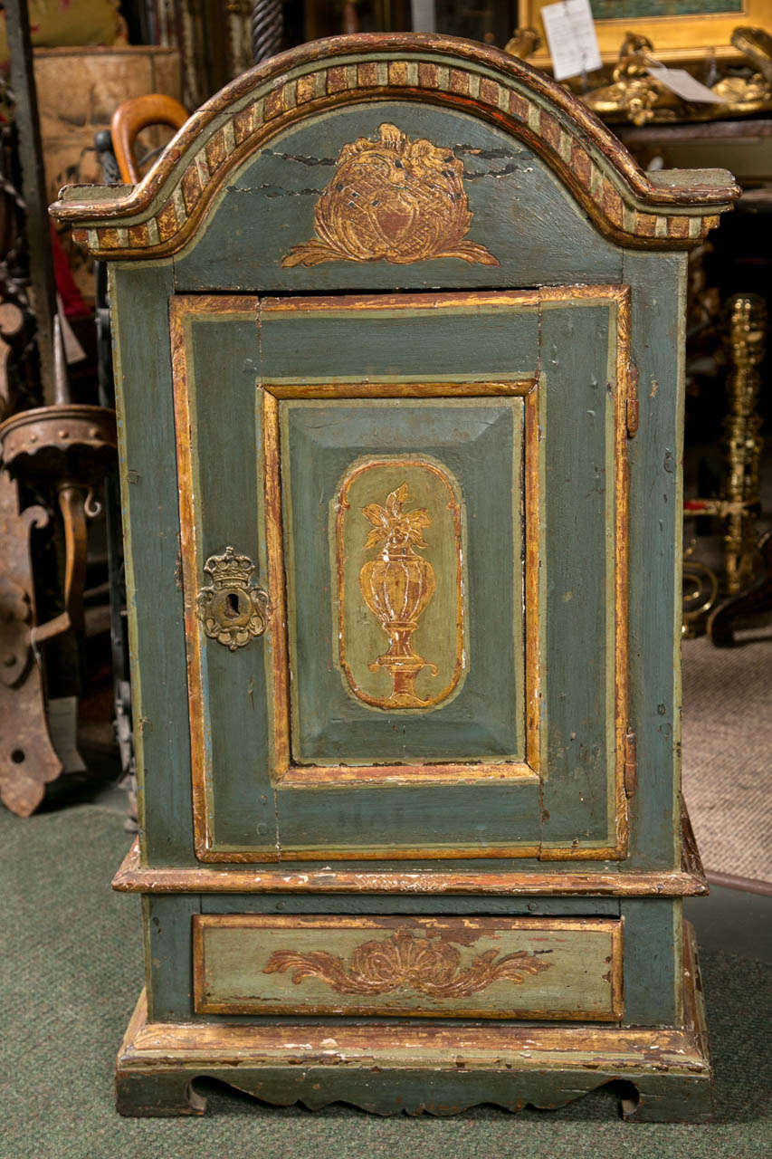 A continental painted cabinet with an arched top, a door opening to a fitted interior and a lower drawer.