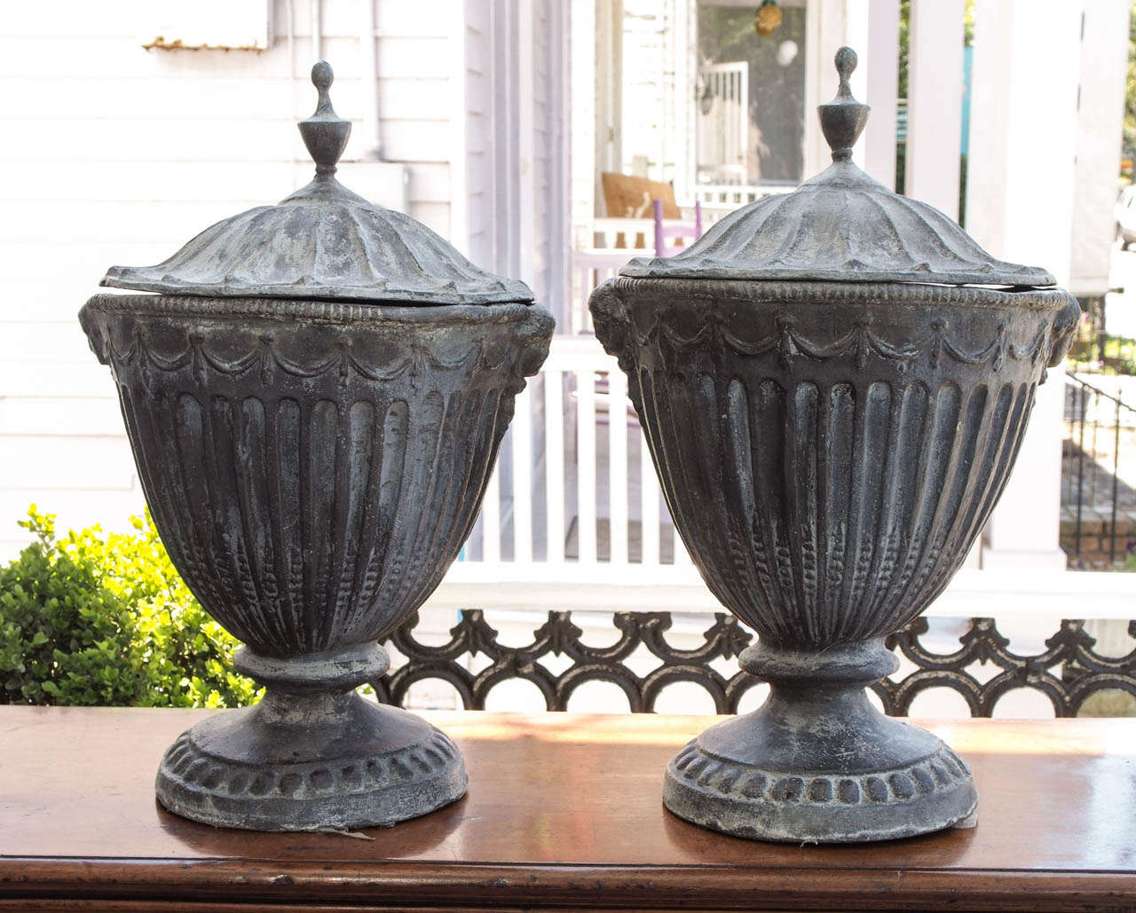 Pair of English Lead Garden Urns with separate covers in the neo classical style.
These are probably English and have rams heads with fluting and gadrooning.
They have some mis shape as they are lead and when they are moved the weight of them