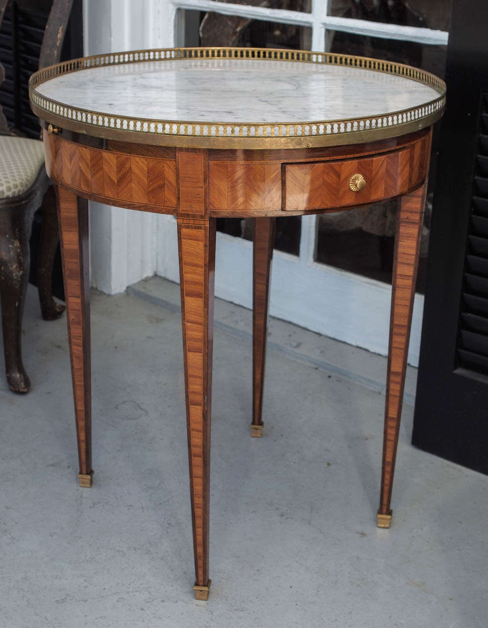 French Marquetry Bouilliotte table with brass gallery and marble top. two drawers and two candle stands pull out with bronze sabot Early 19th c. in the 
Louis XVI style