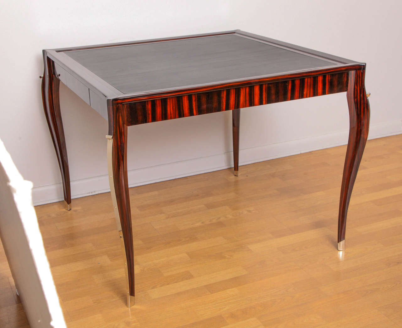 An Art Deco card table with black leather top, macassar ebony and nickel details.