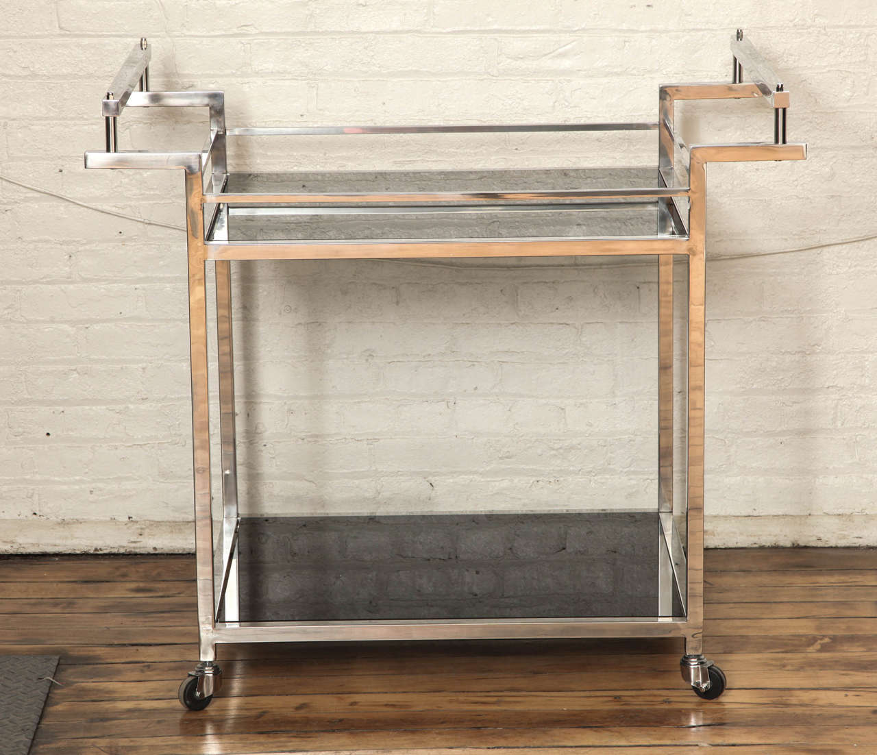 A modernist rolling bar of great proportion. Polished nickel with smoked glass shelves.