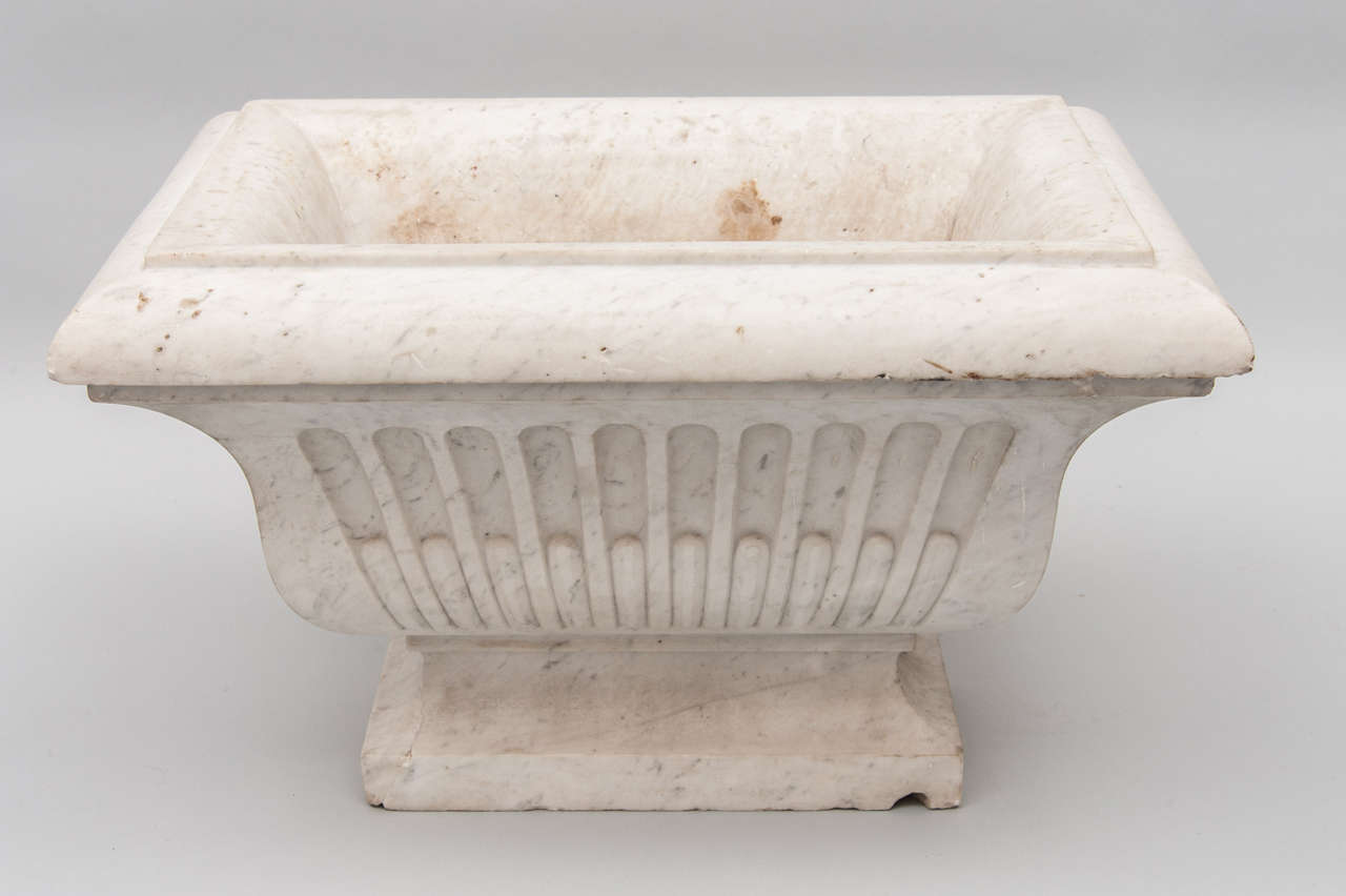 An impressive pair of early 19th century Carrara marble wine cisterns / jardinieres. The rectangular moulded top over fluted and gadrooned shaped body above a stepped socle base.
