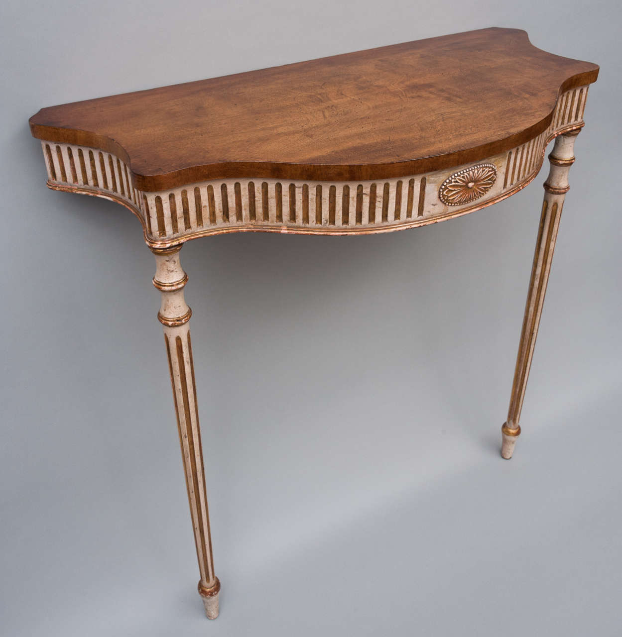Geo III pair of neo classical pier tables of elegant proportions; with serpentine, figured mahogany tops; above a cream and parcel gilt decorated freize with flutes and carved central paterae raised on fluted slender turned legs.
