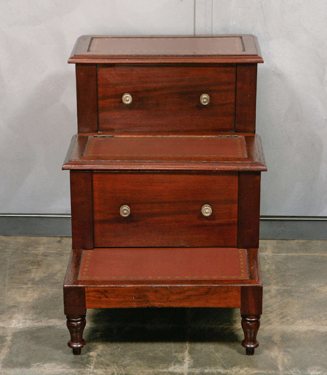 A good GIII Step Commode in excellent condition. Standing on four turned legs the steps have a variety of decorative elements including; three inset tooled leather surfaces in tan, hinged lid element, pull drawer with two brass knobs, other brass
