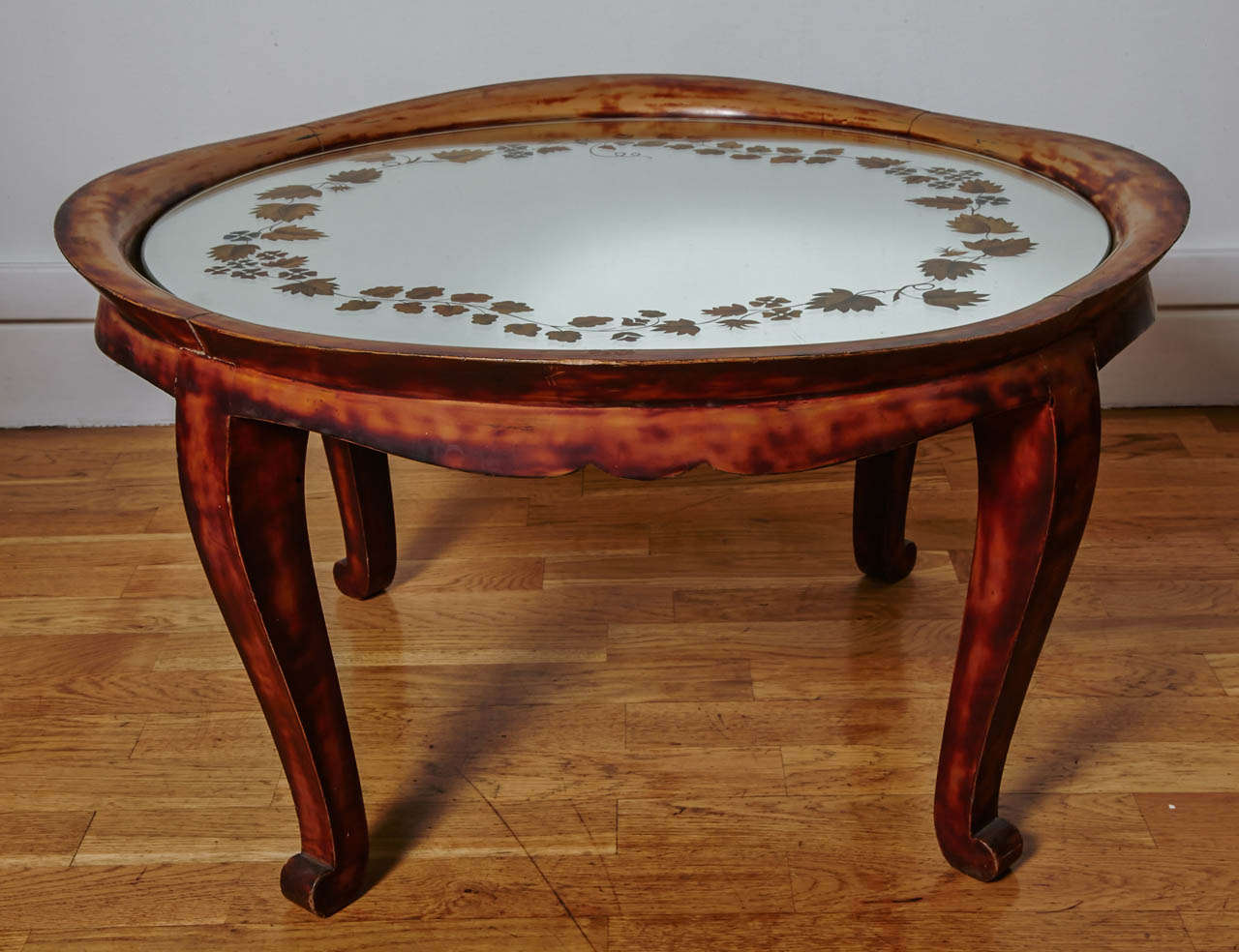 Low coffee table or gue´ridon in irregular turtle-shell color Chinese lacquer. Basin shape top with curved sides. Four shaped legs. Mirror top with a gilded 'e´glomise´' decor of a red and blue flowery branches frieze.

Stamped 'Andre´ Arbus' as
