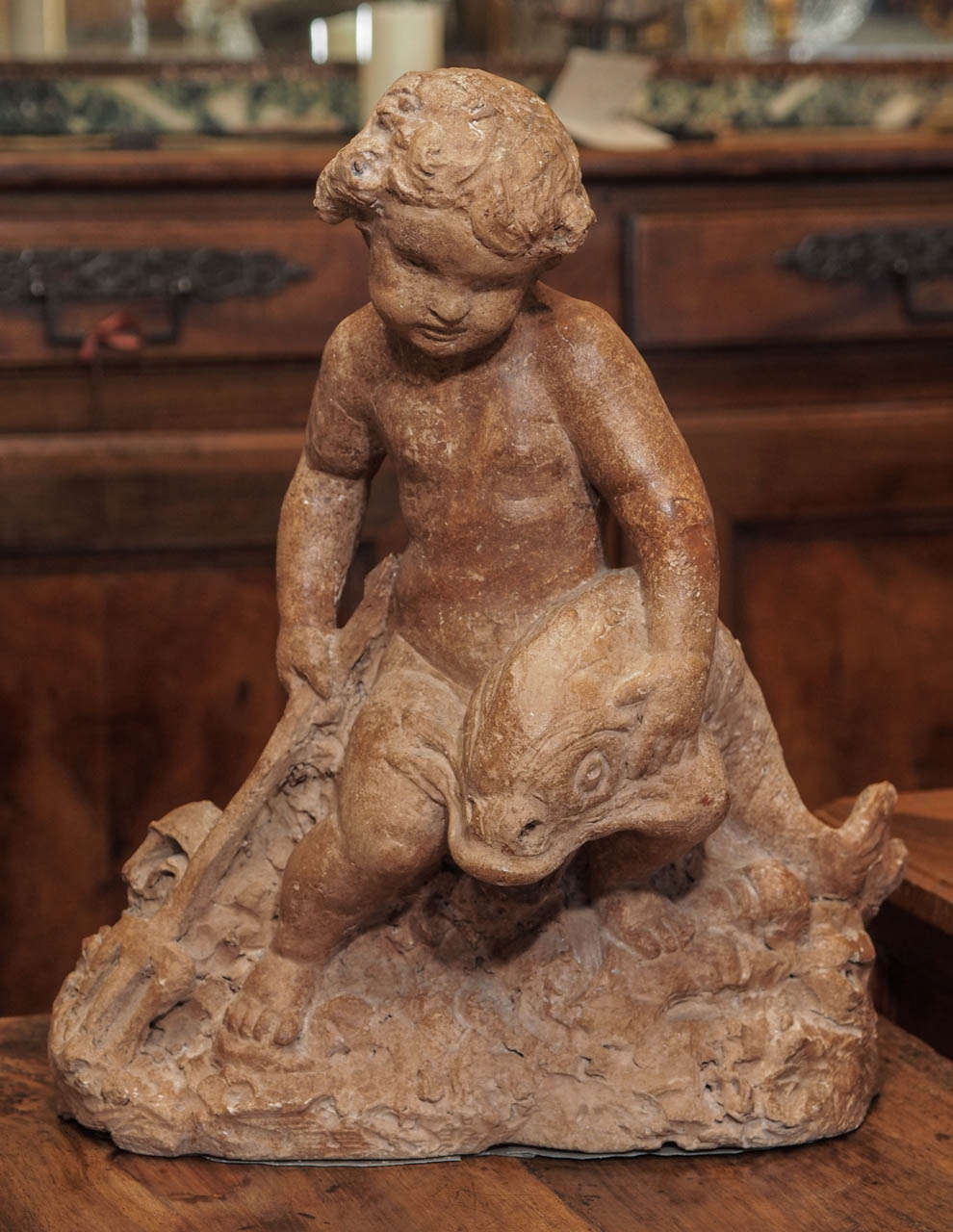 A 19th century French terra cotta statue depicting a putto holding a trident and a dolphin.