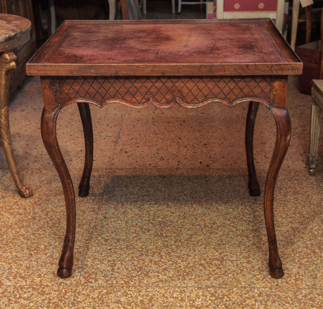 A mid-18th century game table.  The shaped apron carved with a criss cross pattern and pierced by 2 drawers, raised on cabriole legs ending in hoof feet.
Burgundy red leather top (color is uneven).