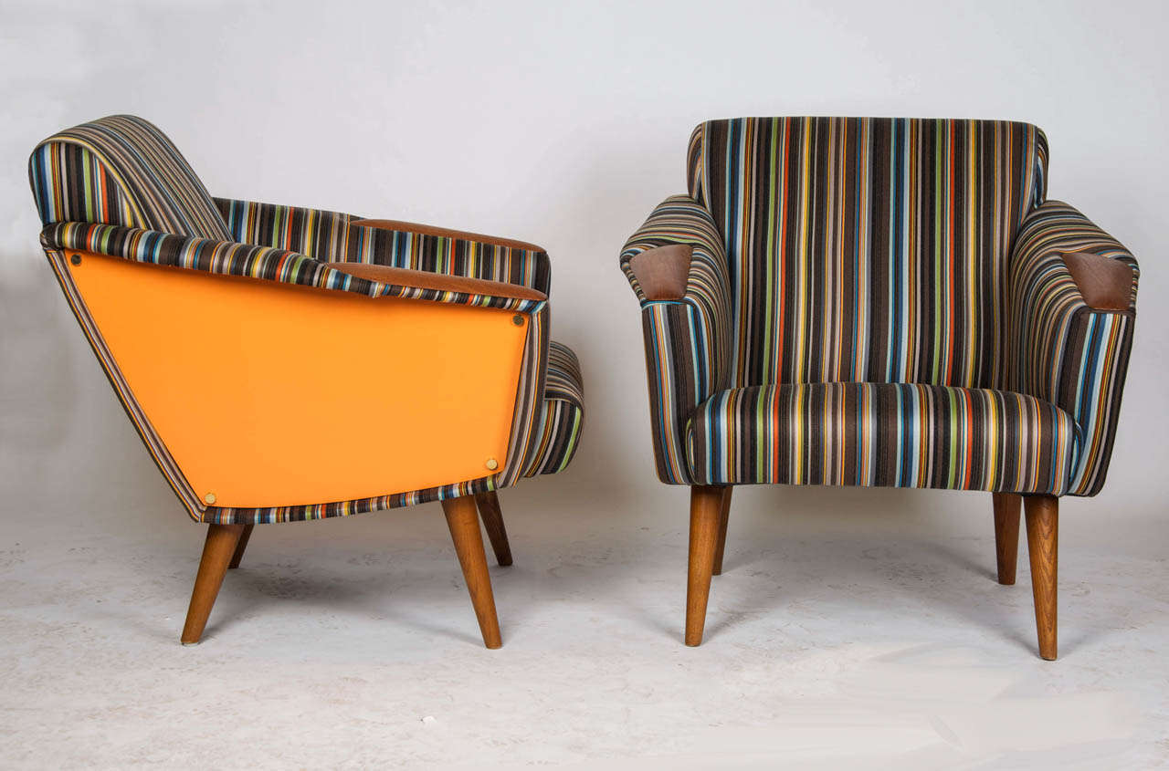 A pair of 1960's Knoll-style arm chairs with teak armrests and feet, recovered in Paul Smith fabric and set with orange veneer to the sides.