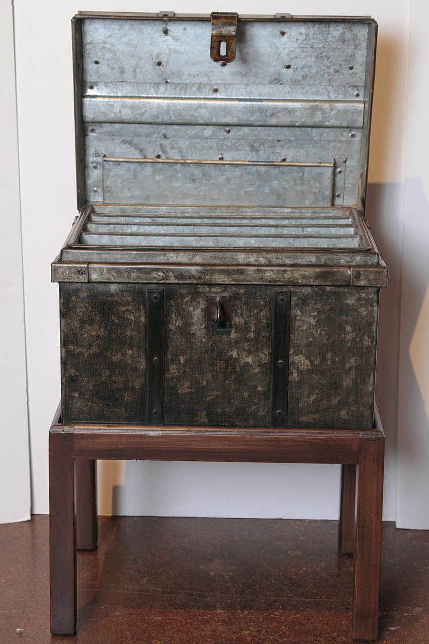 Industrial storage box with stand.
strap design on storage box with patinated steel ebony and bronze coloration on a mahogany wood stand.
Natural grey patina on interior with moveable four component shelf.
Metal hardware with lock