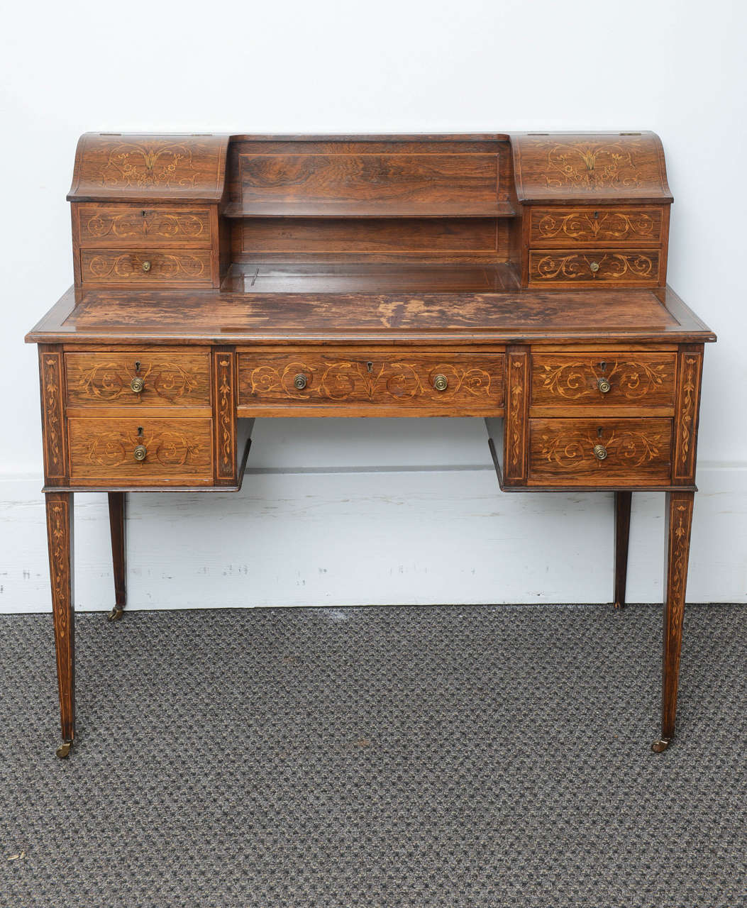 This is a superb rosewood ladies writing desk smothered in satinwood marquetry inlay, in total there are nine drawers four to the top and five to the bottom.
At the top there are two lift up compartments for envelopes and pen holders.
The drawers