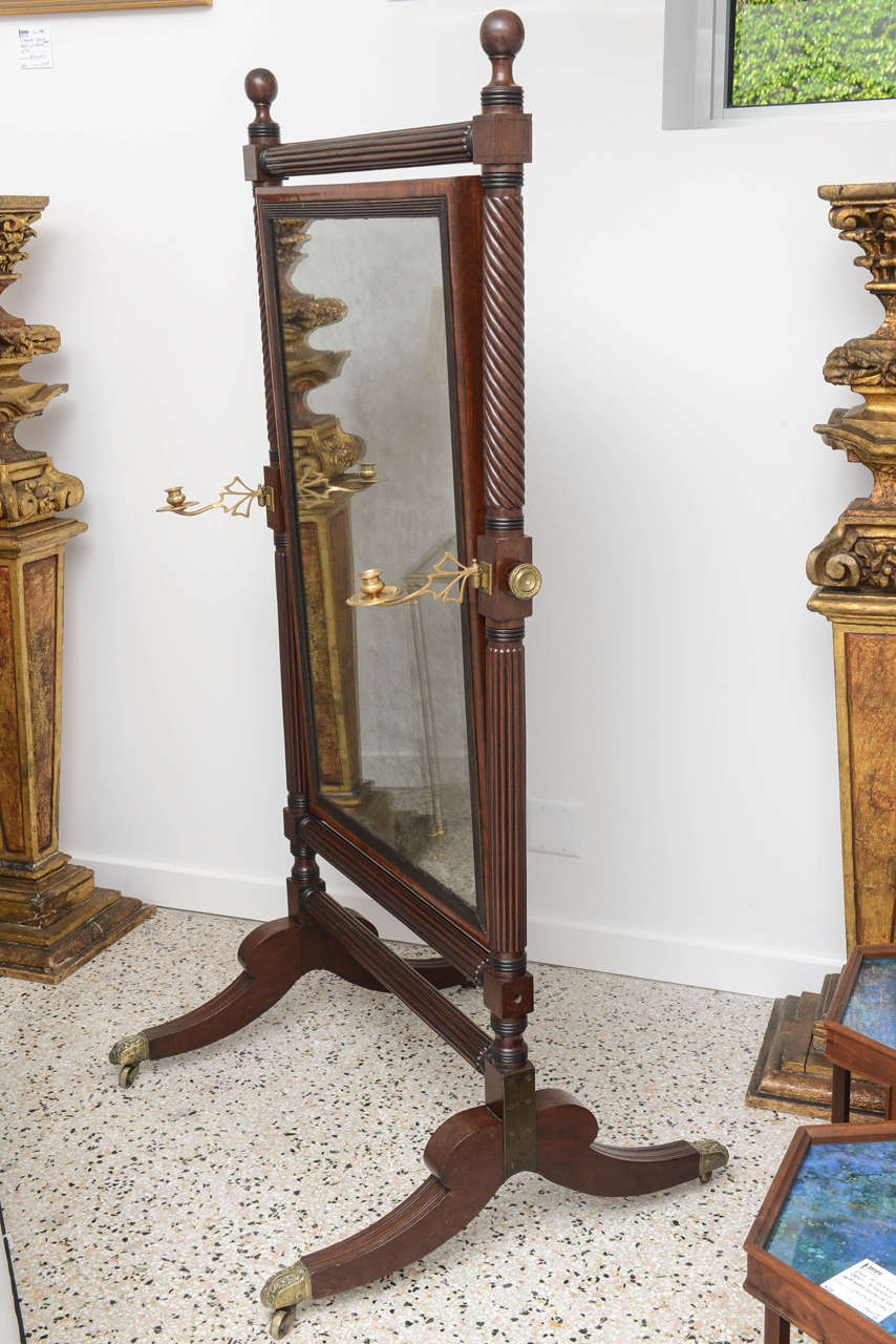 This stylish English, George IV Cheval mirror dates to around 1810 and was purchased from a Palm Beach estate.  The Cheval is fabricated in mahogany wood and retains its original mirror, brass candle holders and stylized acanthus leaf motif