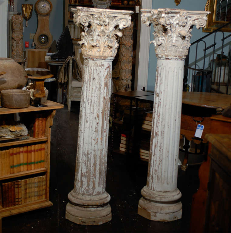 A Pair of 19th Century American Painted Cast Stone Corinthian Capitals over Wooden Short Columns with Crackle Finish on Octagonal Wooden Base. The Capitals are not attached. Each column has a small hook on the center part.

They both have a very