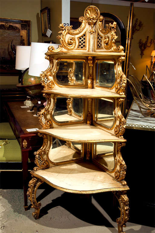 Gilt gold and parcel paint decorated four shelf corner unit. Each shelf has a mirrored back splash. The Louis XV style feet supporing a finely carved upper shelving unit. The piece is carved with gilt gold rosettes and shell form. By Maison Jansen