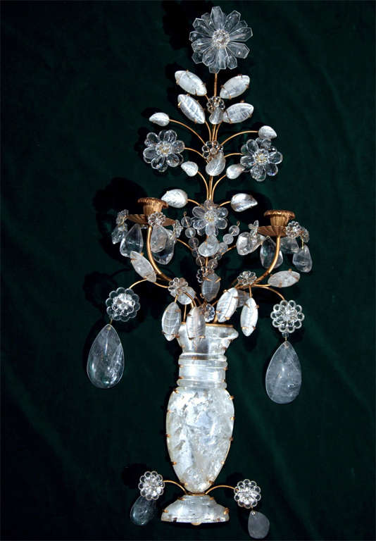In the Baques manner, gold tone metal arms, drip pans and candle cups. large central urn form from which emanates the candle arms and the branches supporting rock crystal flowers and tear shaped drops. Not wired.