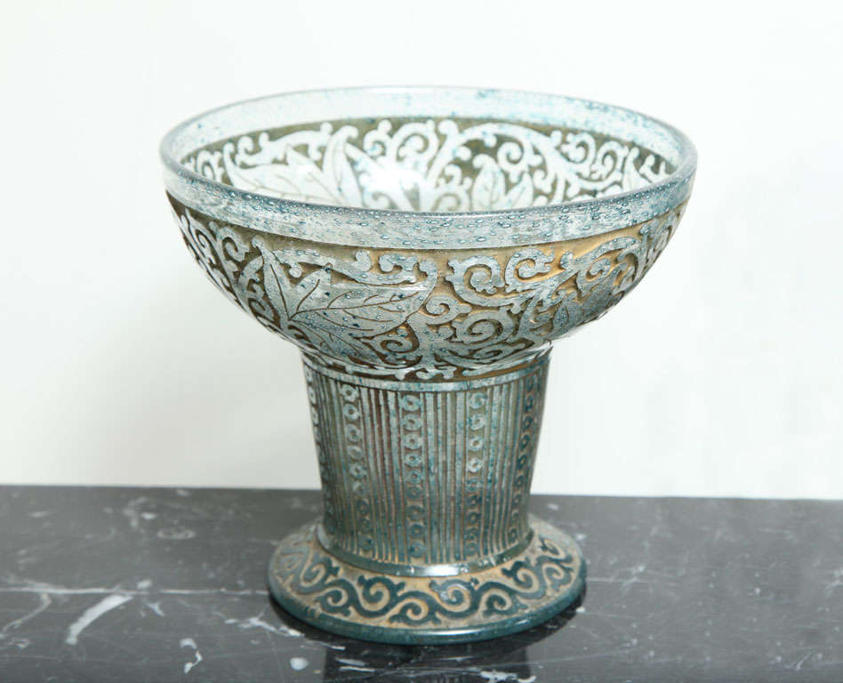 Daum Nancy
Art Deco Footed Vase circa 1920 
Acid etched, blue decorated with foliage and stylized scrolls on a gold backround
Engraved Daum Nancy with Cross of Lorraine along the base
Height: 6 1/2”, Diameter: 7 3/8”