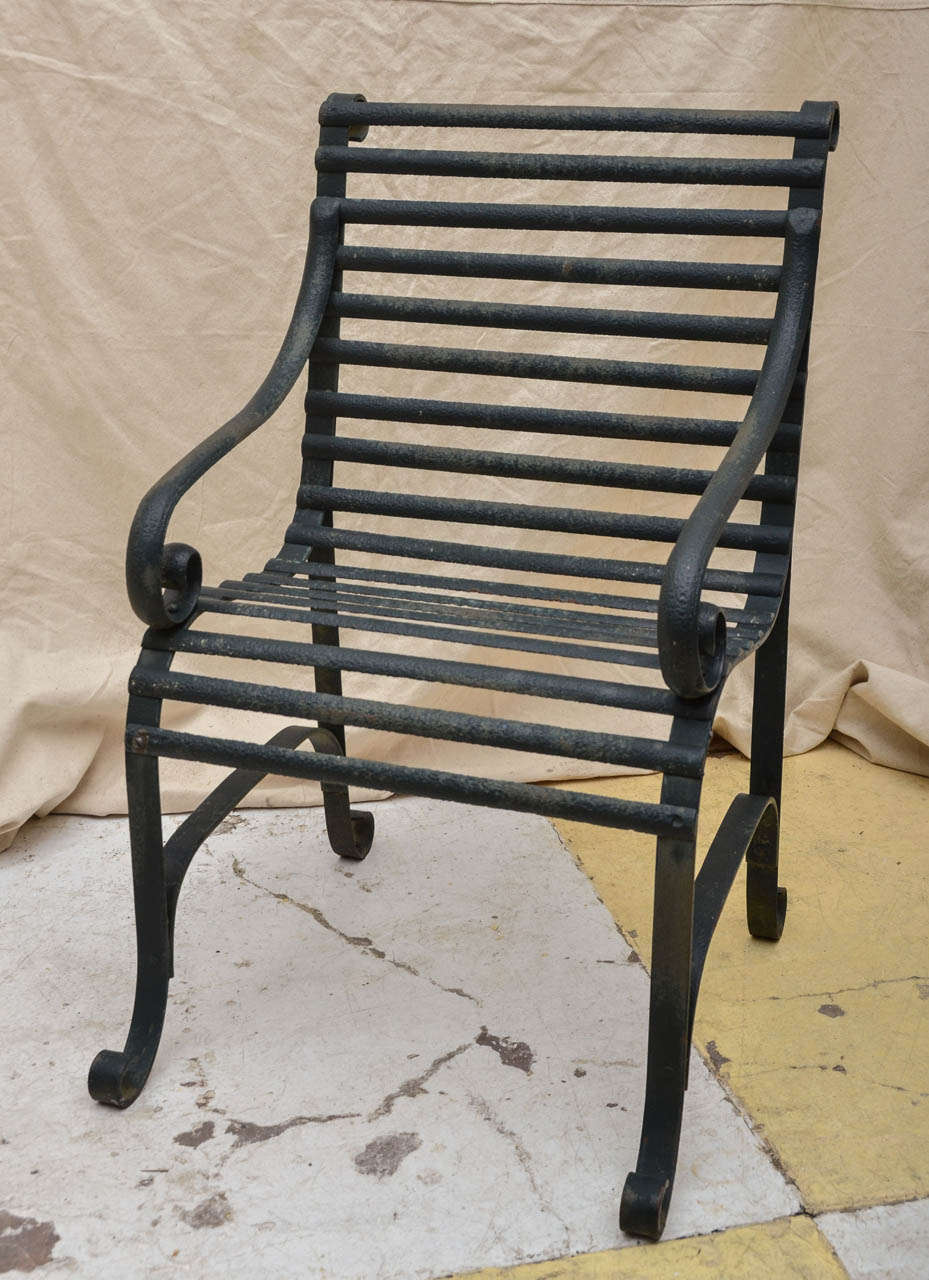 English Regency wrought-iron garden chair composed of scroll-arm supports, legs and back supports joined by half round slats in old forrest green paint. A classic garden chair, quite comfortable and very heavy, also nearly indestructible.