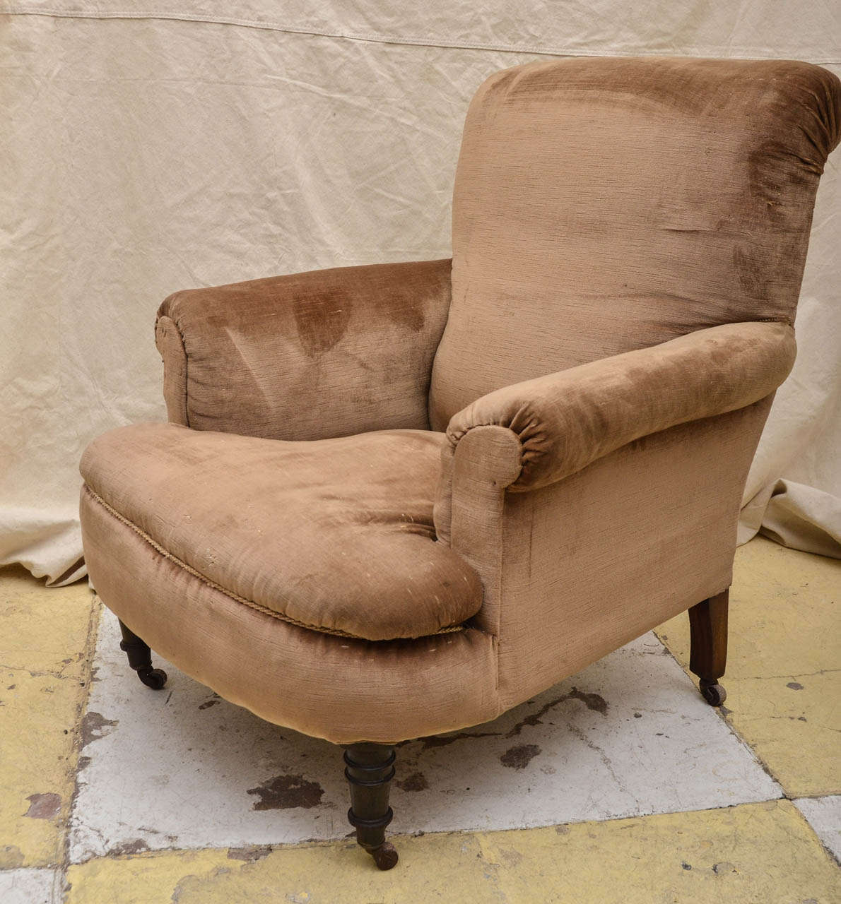 English Late 19th Cent. Howard Style Club Chair On Turned Circular Front Legs And Tapered Rectangular Rear Legs With Brass Castors Having Brown Ceramic Wheels. The Upholstered Seat Of The Chair Has A Bow Shape With Out Swept Arms & Back. A Very