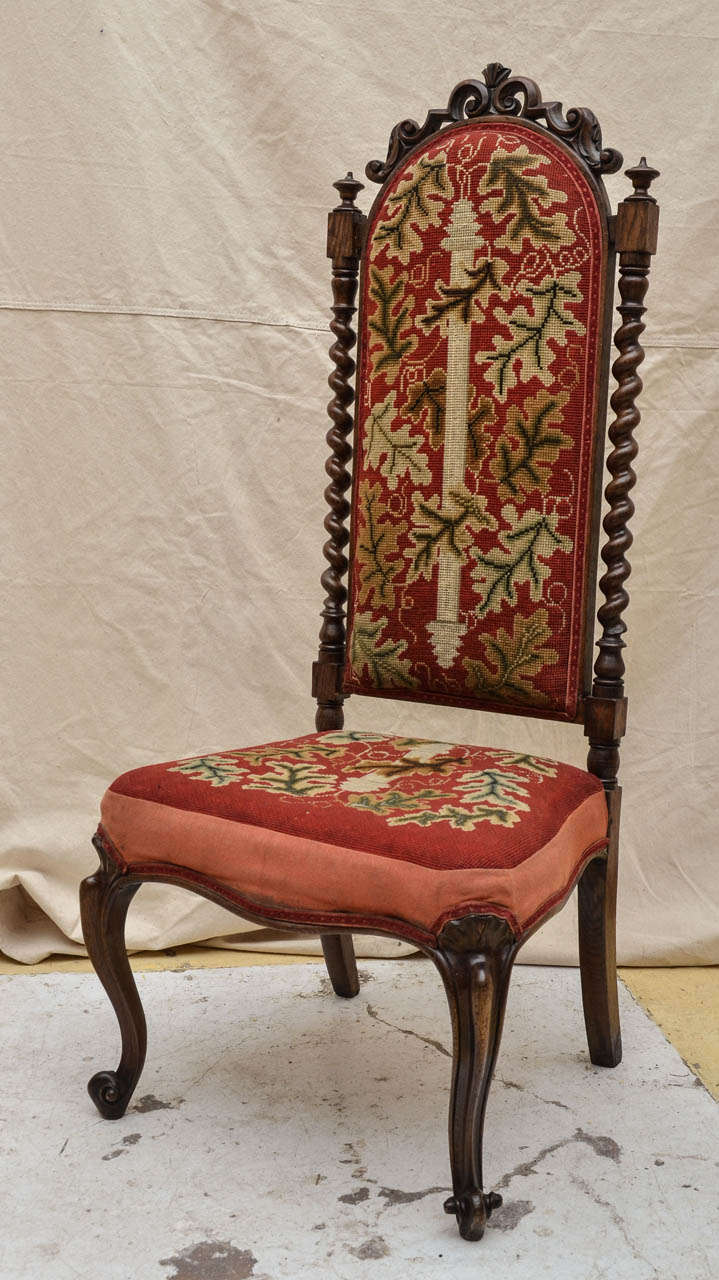 19th Century English oak tall-back needlepoint-covered accent chair with barley twist spindles to the sides of the back, topped by a scroll cutout crest. French design cabriole front legs. needlepoint in a deep rich red background, centered by a