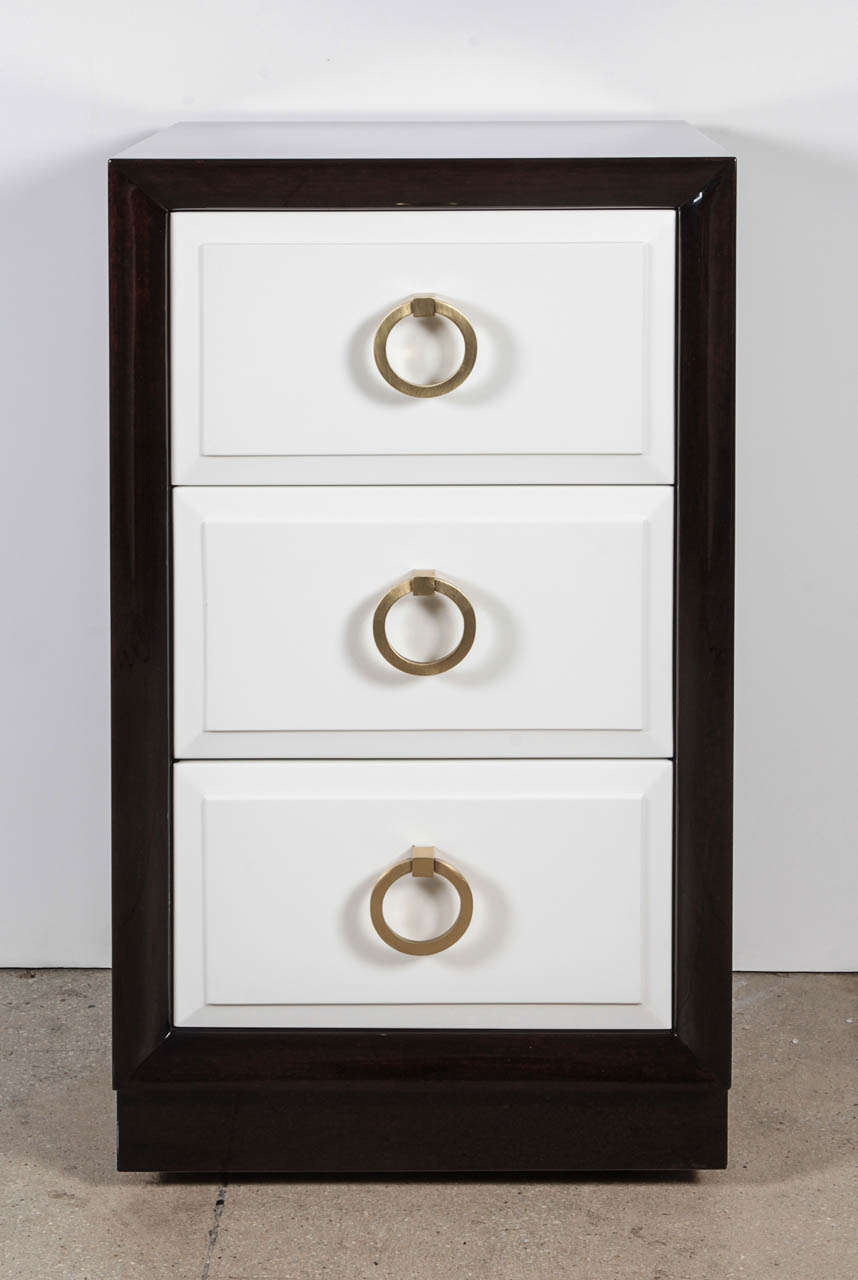 Pair of Mid-Century Classic nightstands with an ebonized walnut case and matte paper white lacquer fronts featuring satin brass door knocker pulls. Designed by TH Robsjohn Gibbings for Widdicomb.