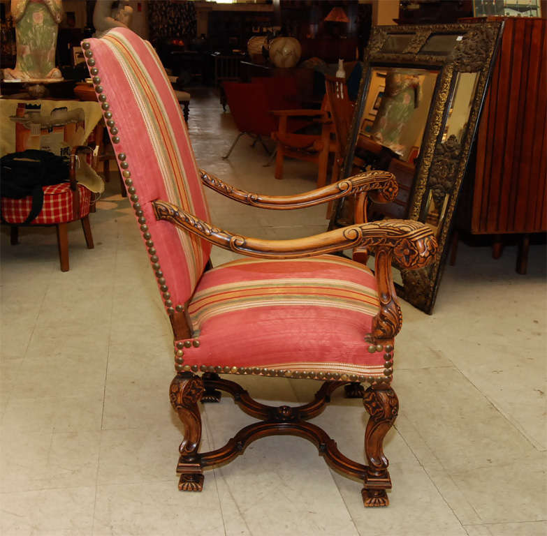Tall-backed French provincial style armchair in oak, with exaggerated carved arms and cabriole legs and bold metal-studded upholstery