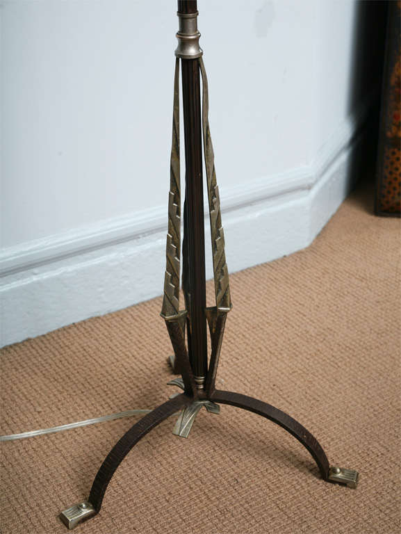 An Art Deco floor lamp having shaft of fluted iron supported by pointed braces of nickel on arched tripod legs ending in nickel feet.