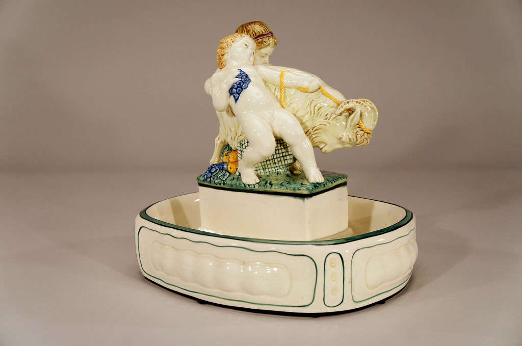 A large and whimsical Weiner Werkstaate-style pottery centerpiece with two figures and ram atop the trough shaped centerpiece. The cream colored enamel body is embellished with a naturalistic polychrome enamel decoration. The children's figures are