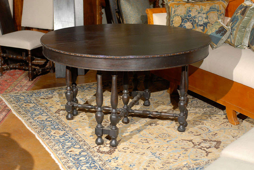 A French dark wood round dining table with unusual turned legs and five leaf extensions, perfect to accommodate from four to eight people. This French dining table features a circular top with discreetly carved molding over a solid apron. The table
