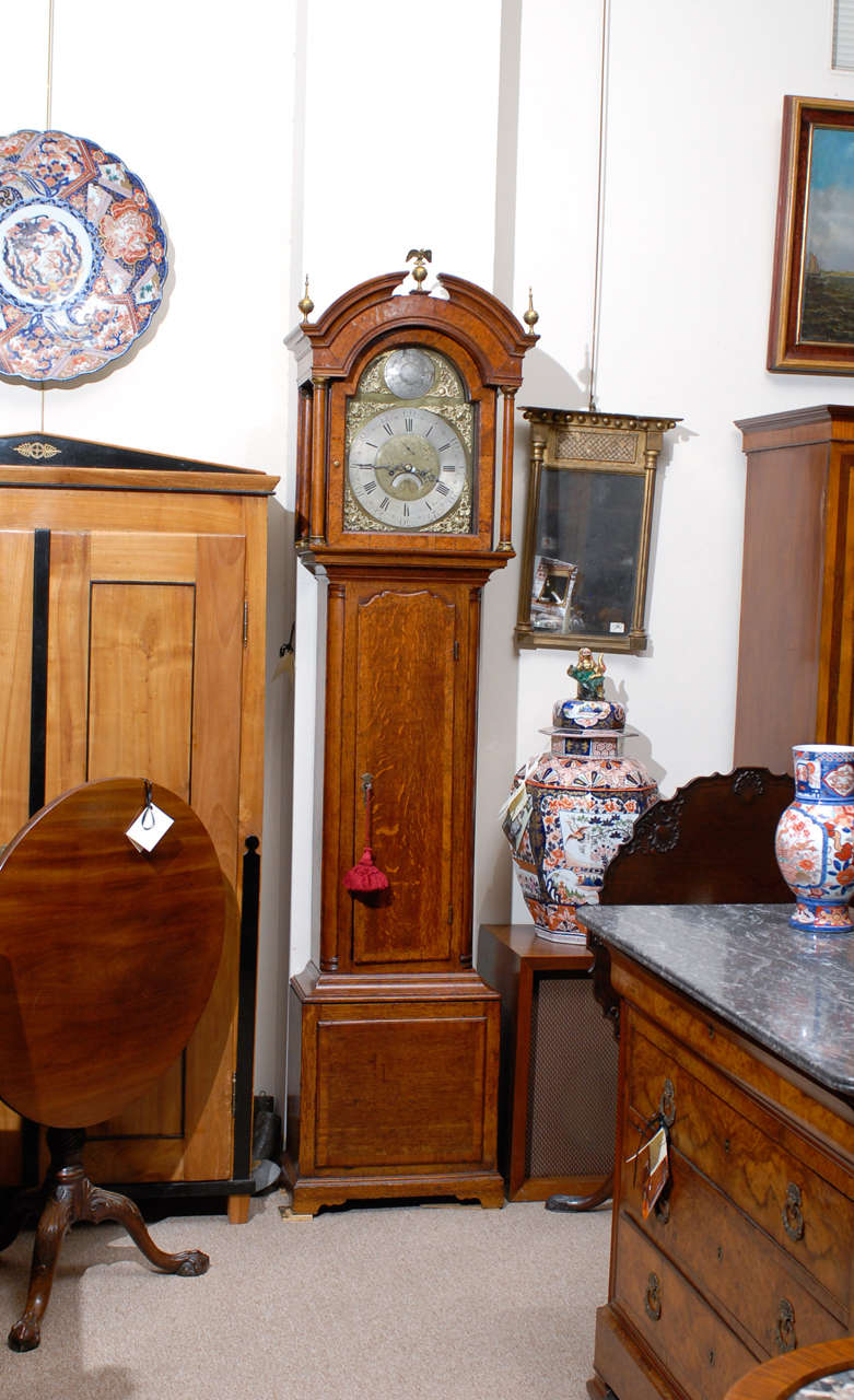 A tall case clock in oak with broken arched pediment, brass finials, brass face and flanking column supporting face, the dial signed 
