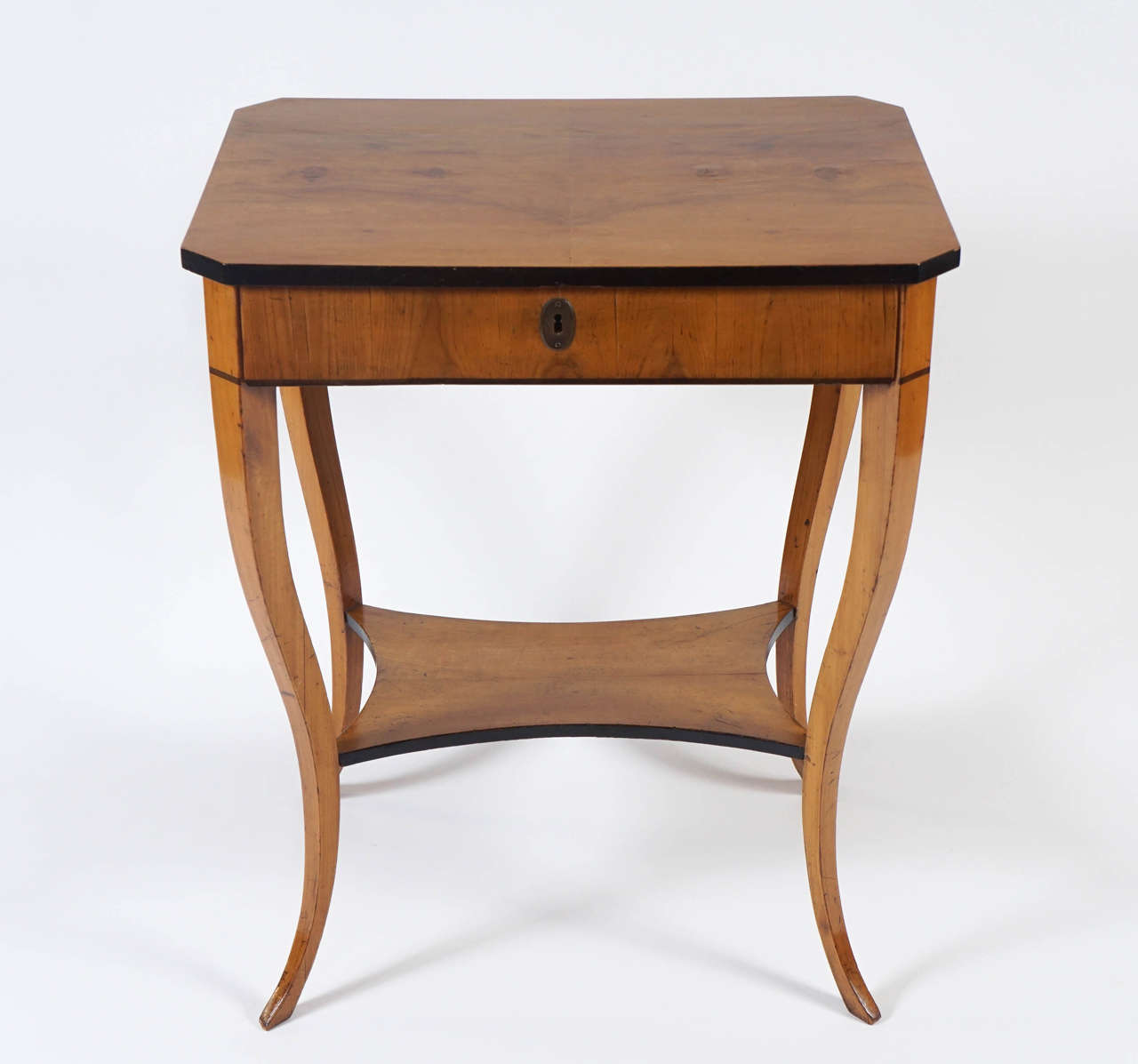 Elegant early Austrian Biedermeier period walnut occasional table or Stand having rectangular top with canted corners and ebonized edges surmounting single drawer with original oval brass escutcheon on gently undulating splayed legs joined by a