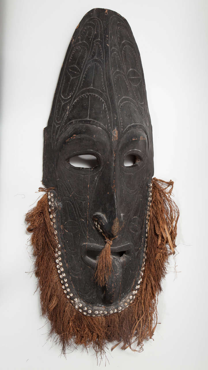 A striking tribal mask with a beard of natural fibers that add a human quality to the starkness of the wood.