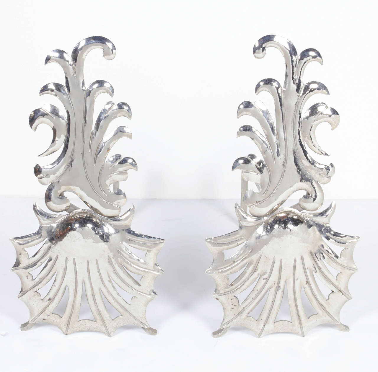 Pair of elegant fireplace andirons with stylized shell design and wave patterns. Polished nickeled finish over steel and cast iron. Featuring hand-forged and hand pierced eclectic Hollywood Regency design.