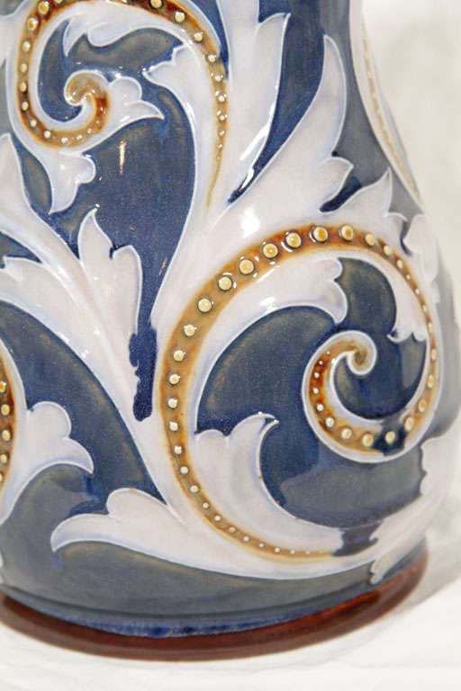 This late 19th century Saltglazed stoneware jug is decorated in tones of blue, brown, and white with incised leaftips and large applied beading and rosettes. The handle is ear shaped.

In 1815 the company founder, John Doulton, began producing