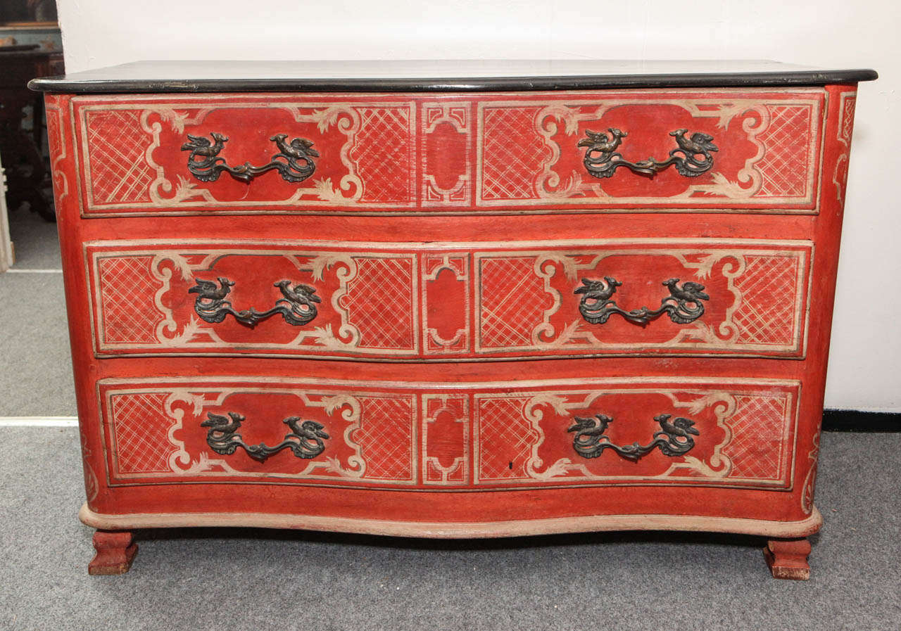 Vibrant, hand carved and painted, three-drawer, serpentine front, faux paneled, crimson, French commode with period, brass handles. The whole decorated in a lattice-work pattern Surmounted bya black, faux marble-top.