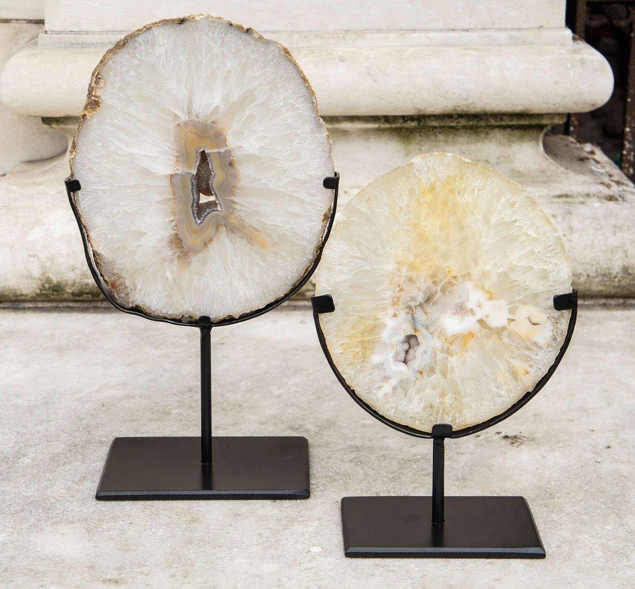 These two natural geode slices have been mounted on custom iron bases. The slices have been cut thickly and fully polished but still allow light to play through the surface showing the development of the geode and both have the central crystal