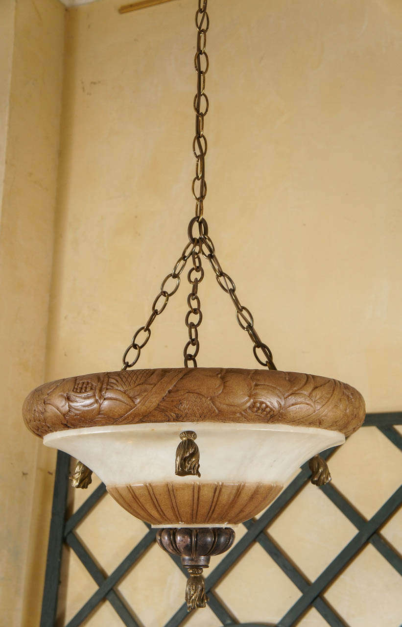 This carved alabaster bowl fixture from the early Art Deco period is in two colors natural and almond. All the external mounting parts such as tassels and lower drop finial are crafted in silvered bronze and have been left in the natural patina with