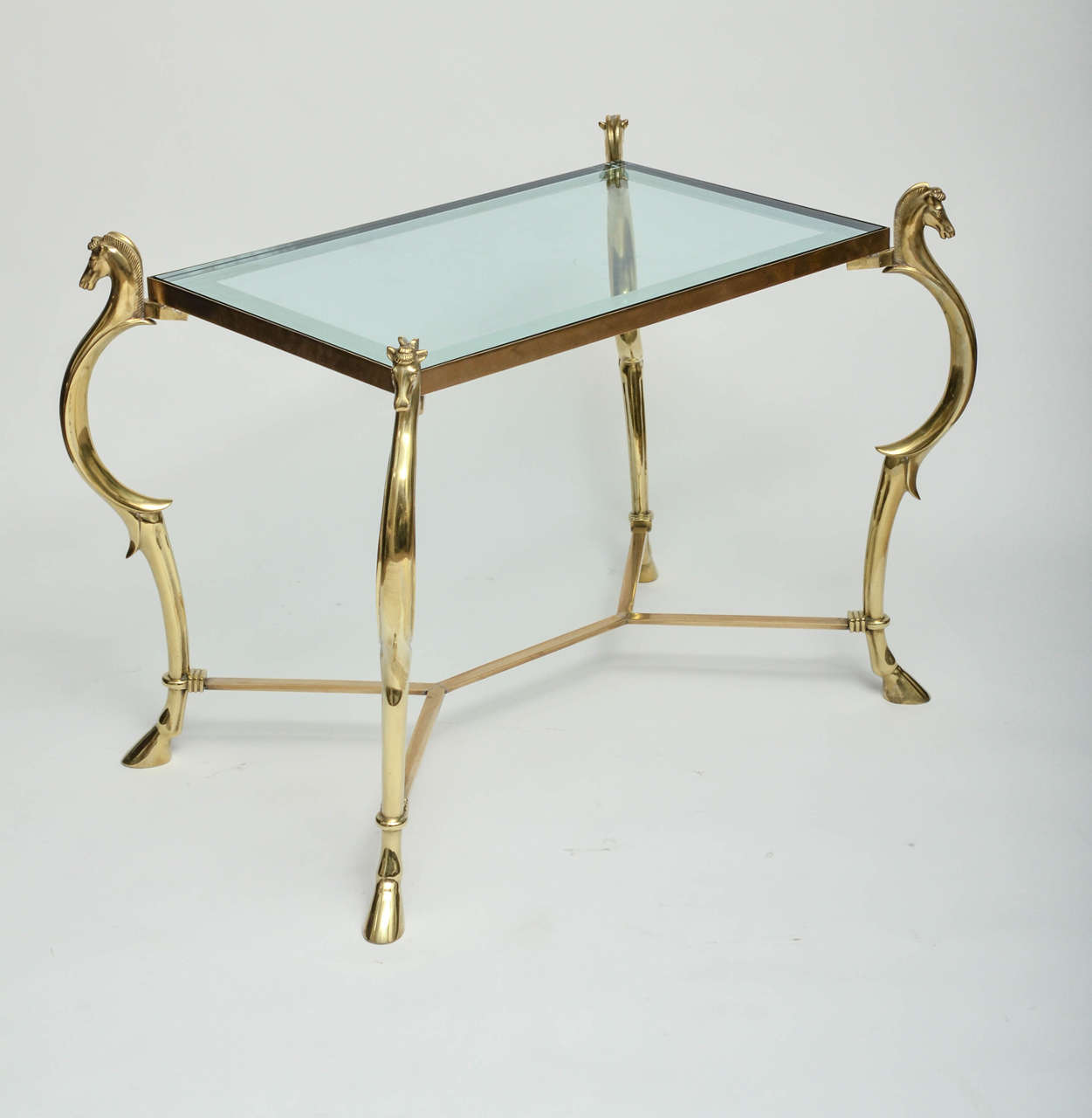 Pair of curvilinear brass side tables with horse head finials and mirror trim glass tops.