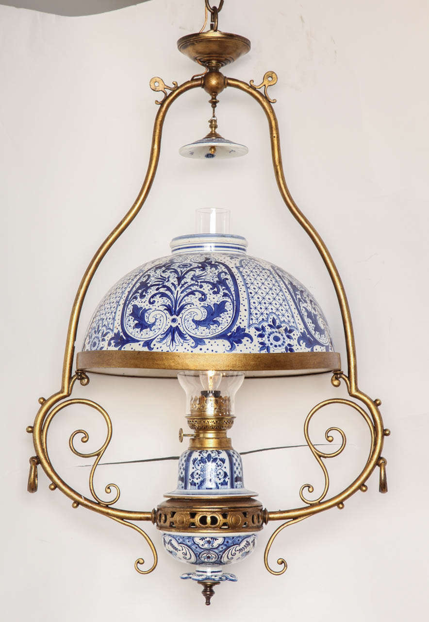 A single light Dutch delft fixture with gilt bronze frame having delft oil reserve, oil fittings, and hurricane shades. The light partially concealed by Delft dome with smoke bell.